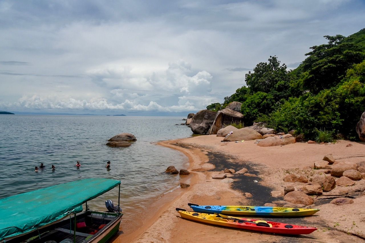 A sandy cove with swimmers, kayaks and a moored boat